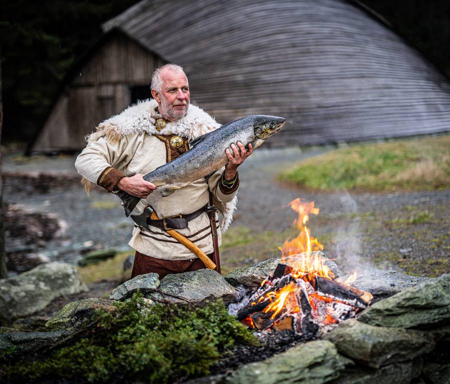 Mann med hel laks ved et bål hos Skakke Røykeri